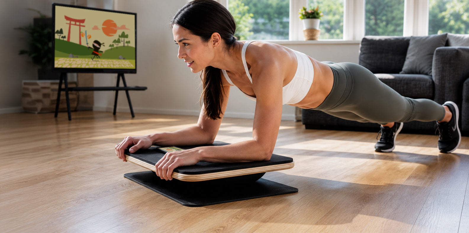 A woman does a plank exercise on a Plankpad balance board in front of a smart TV with a gaming app